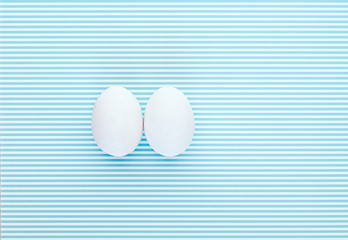 Two eggs on a colorful white and blue striped background. Creative design, minimal concept....