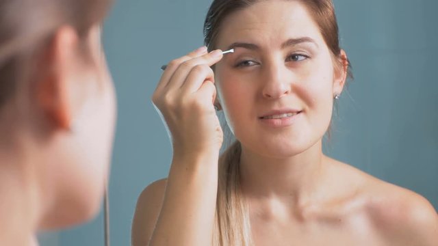 4K footage of young beautiful woman plucking eyebrows at mirror in bathroom