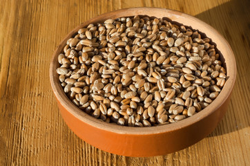 Grains of wheat in a clay bowl on a wooden background texture. Selective focus.