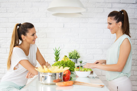 Happy young twin sisters preparing organic vegetables salad for lunch together in the kitchen.