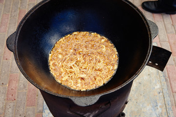 National Uzbek dish pilaf, pilaw, plov, rice with meat in big pan. Cooking process, open fire. Cooking in a cauldron on fire. 
Preparation stages. Onions roasting to color of caramel