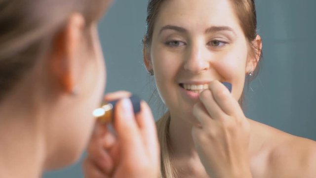Closeup 4K footage of beautiful young woman applying red lipstick at mirror in bathroom