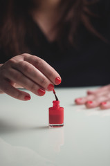 Woman is painting her nails with red nail polish