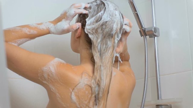 Slow motion video of brunette woman washing long hair with shampoo