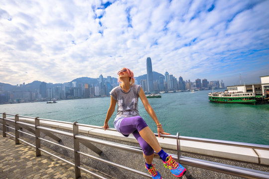 Enjoyment Caucasian Woman With Urban Background Hong Kong Skyline. Female Fitness Athlete After A Workout On Tsim Sha Tsui Promenade In Victoria Harbour, Kowloon. Healthy Lifestyle Concept.