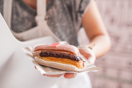 Female saller holding eclairs to the bayer at market. Soft selective focus, close up
