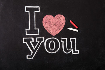 Black chalkboard with text I love you and chalks