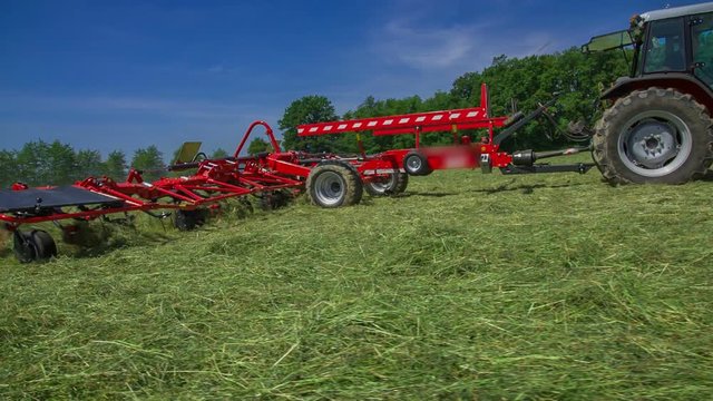 Farmers are very busy in the summer time. They are preparing hay on large fields with rotary rakes machinery.
