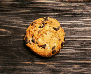 Tasty cookie with chocolate chips on wooden background