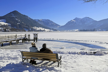 Winterlandschaft: Paar auf einer Bank am See mit Bergblick 