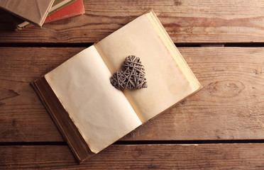 Old open book and decorative heart on wooden background, top view