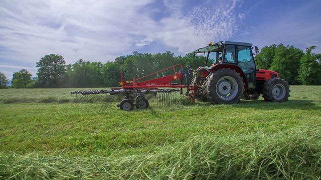 A farmer is driving a tractor on a large field and he is organizing hay in different lines.
