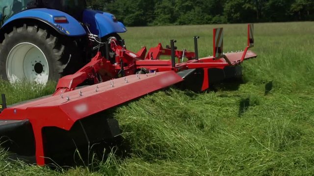 Grass is coming out of the machine when a farmer is sitting on a tractor and he is cutting grass with a grass cutting machine.
