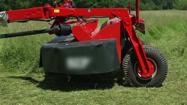 We can see wheels of the grass cutting machine slowly moving. A farmer needs to change direction a bit. He is cutting grass on a large grass field.
