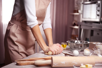 Young woman making dough in kitchen