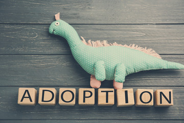 Cubes with word ADOPTION and dinosaur toy on wooden background