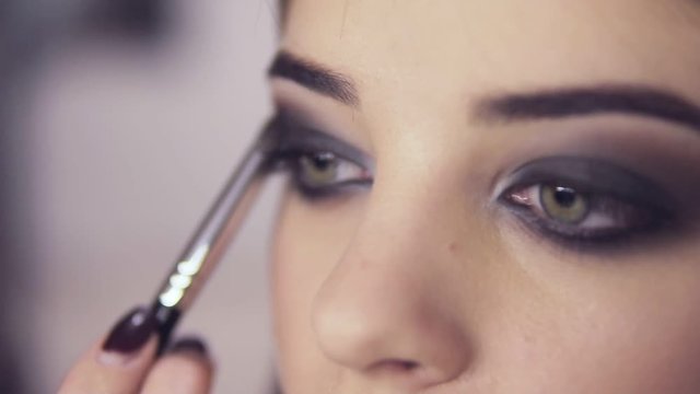 Make-up artist applying eye shadow makeup to model's eye. Close up view. Smoky eyes. Right view