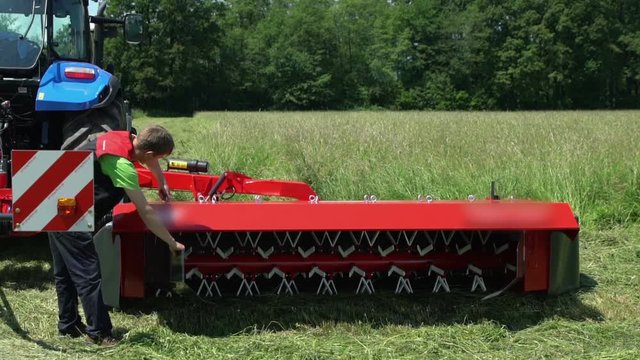 A young man is checking if everything is working properly. He is fixing something on the grass cutting machine.
