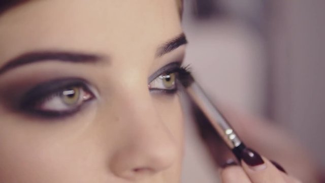 Make-up artist applying eye shadow makeup to model's eye. Close up view. Smoky eyes. Left view