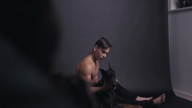 Backstage of photo session of young half naked man with doberman in studio