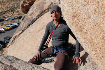 Young south asian woman dressed for cold weather rock climbing kneels with gear slung over her...