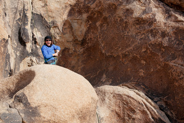Naklejka premium Young caucasian woman dressed for cold weather rock climbing in the desert climbs a cliff. Wearing a jacket, hat, and glasses