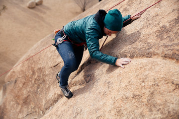 Young caucasian woman dressed for cold weather rock climbing in the desert climbs a cliff