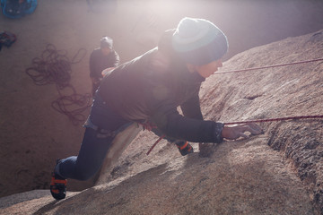 Young african american woman dressed for cold weather rock climbing in the desert climbs a cliff