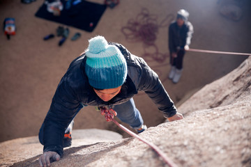 Young african american woman dressed for cold weather rock climbing in the desert climbs a cliff