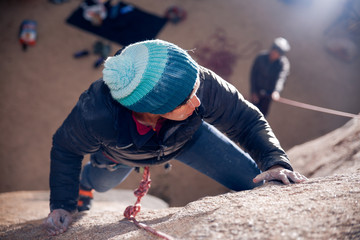 Young african american woman dressed for cold weather rock climbing in the desert climbs a cliff