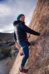 Fototapeta premium Young african american woman dressed for cold weather rock climbing in the desert climbs a cliff and smiles at the viewer