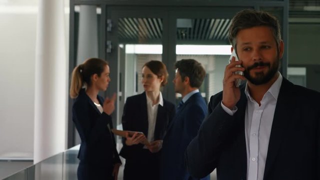Businessman talking on mobile phone in office while colleagues discussing on background 4k