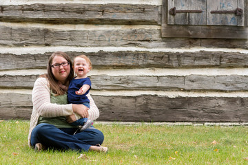 Happy mother and daughter sitting in the grass in front of an old house