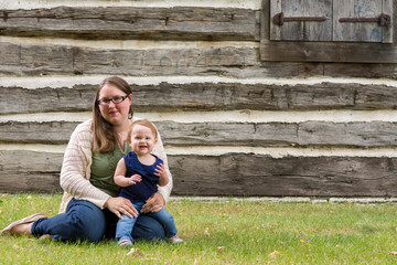 Happy mother and daughter sitting in the grass in front of an old house