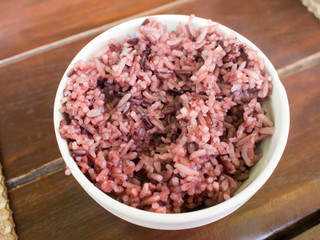 Coarse rice in a white bowl on wooden background.