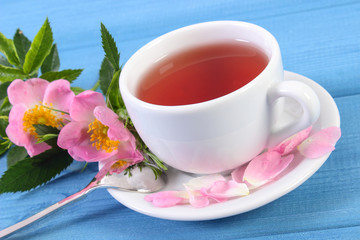 Cup of tea and wild rose flower on blue boards
