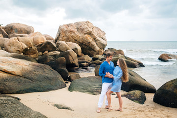 young couple in love in blue shirt holding hands on the beach and looking at each other. Sea big stones background. Concept of family