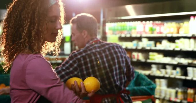 Smiling female staff arraigning sweet lime in crate at organic section of supermarket 4k