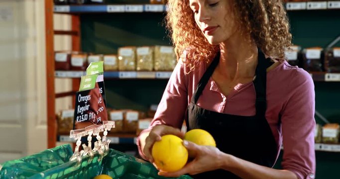 Smiling female staff arraigning sweet lime in crate at organic section of supermarket 4k