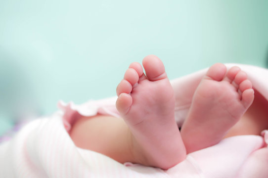 Premature baby feet with little toes, pink blanket, and turquoise background
