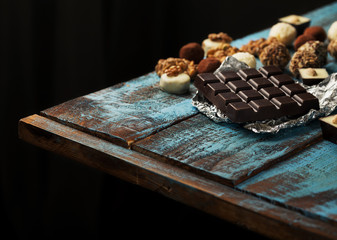 Dark chocolate bar with different chocolates on wooden table