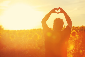 Farmer at sunset in the field, heart shape hands.