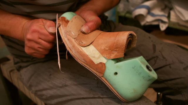 Cobbler cutting a piece of leather on shoe last