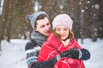 Obraz premium The guy embraces the girl and covers it with a warm blanket in the winter forest, couple of lovers
