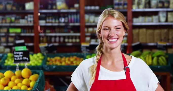 Portrait of smiling female staff standing with hands on hip in grocery section of supermarket 4k