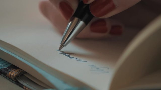 Close up female hand with red nail polish writing cursive with ball pen on plain white paper 4k