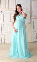 Young smiling beautiful pregnant woman in blue loose dress