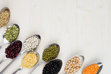 Decorative border of assortment pulses beans in  spoons with copy space on white wood background. Top view, closeup. - obrazy, fototapety, plakaty