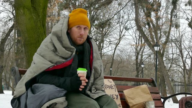 
4K. Adult  homeless poor man  on  winter city bench  drink coffee, tea
