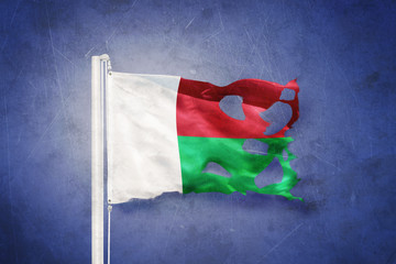Torn flag of Madagascar flying against grunge background